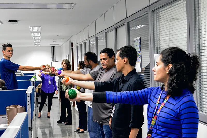 Trabajadores hacen una pausa activa en su oficina: brazos extendidos y pelotas de masaje, guiados por un instructor.