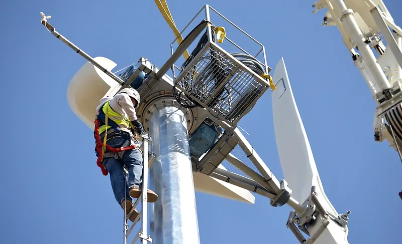 Técnico con arnés de cuerpo completo y casco asegurado en lo alto de una torre metálica.